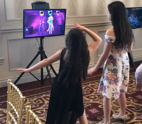 Two girls dancing in front of a dance game screen
