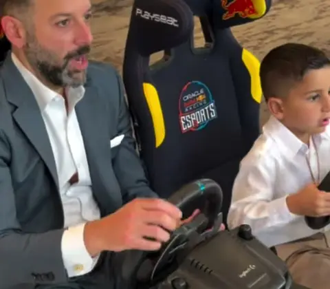 Father in a suit racing next to his son in sim seats